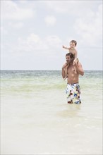 Father carrying son on shoulders in ocean. Date : 2008