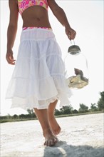 Girl on beach carrying jar of shells. Date : 2008