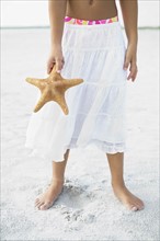 Girl on beach holding starfish. Date : 2008