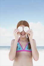 Girl on beach holding sand dollars over eyes. Date : 2008