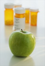 Close up of green apple with prescription bottles in background.