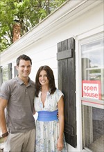 Young couple posing in front of house with ”Open House” sign. Date : 2008