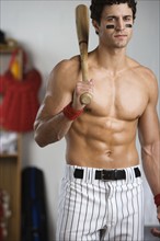 Portrait of baseball player with bare chest holding bat in locker room. Date : 2008