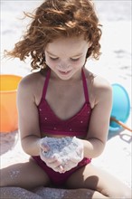 Girl in bikini cupping sand on beach. Date: 2008