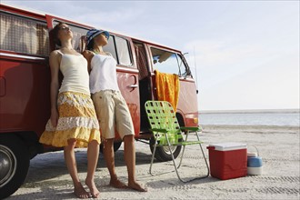 Young women leaning against van on beach. Date : 2008