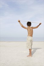 Boy standing on beach holding bodyboard overhead. Date : 2008