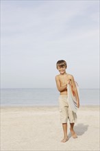 Portrait of boy holding bodyboard on beach. Date : 2008