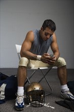 Football player looking at cell phone in locker room. Date : 2008