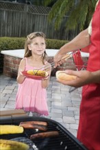 Father at barbecue grill serving daughter hot dog. Date: 2008