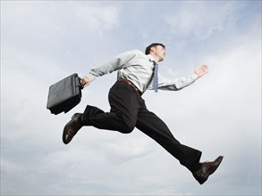 Businessman with briefcase jumping in mid-air. Date: 2008