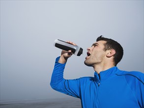 Man drinking from water bottle on foggy beach. Date: 2008