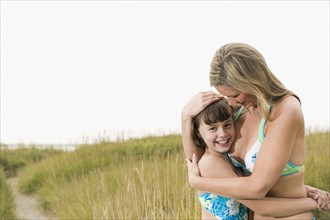 Portrait of mother hugging daughter on beach. Date: 2008