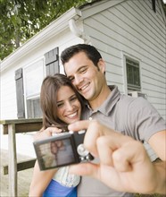 Couple taking self-portrait in front of house. Date : 2008