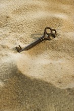 Close up of old-fashioned key in sand.
