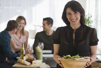 Portrait of woman holding salad bowl with friends in background.