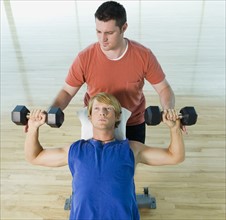 Personal trainer spotting man with dumbbells. Date : 2008