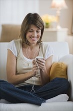 Woman sitting on sofa and listening to mp3 player.