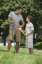 Boy helping father with sprinkler in backyard.
