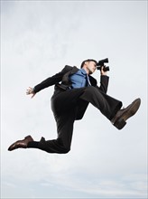 Businessman with binoculars jumping in mid-air. Date: 2008