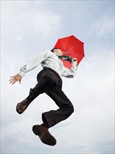 Businessman with umbrella jumping in mid-air. Date : 2008