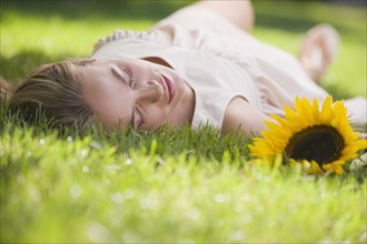 Woman laying in grass with sunflower.