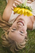 Woman laying in grass holding sunflower.