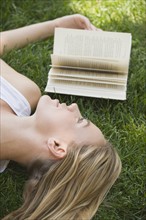 Woman laying in grass with book.