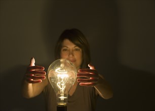 Woman holding hands around large light bulb.