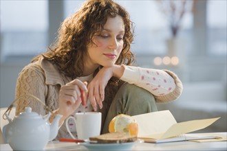 Woman reading letter and stirring tea.