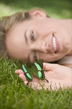 Close up of woman laying in grass holding butterfly.