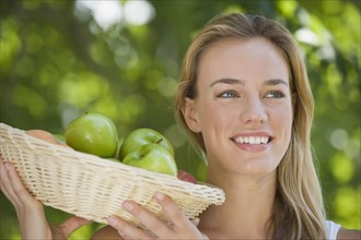 Close up of woman holding basket of apples.