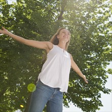 Woman with arms outstretched standing under tree.