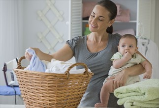 Mother holding baby son and sorting laundry.