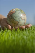 Close up of hand holding globe in grass.