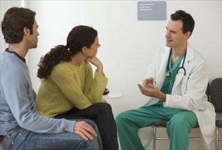 Male doctor talking to couple in waiting room.