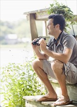 Man sitting on steps of deck with binoculars. Date: 2008