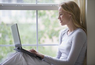 Woman using laptop on windowsill.