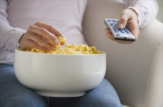 Close up of woman with remote control and bowl of popcorn.