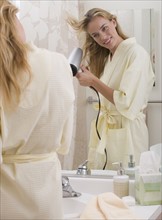 Woman blow-drying hair in bathroom.