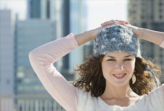 Portrait of woman in stocking cap with city in background.