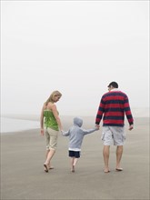 Parents holding hands with son on beach. Date : 2008