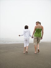 Mother and daughter holding hands and walking on beach. Date : 2008