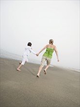 Mother and daughter holding hands and running on beach. Date : 2008