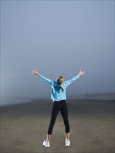 Woman with arms outstretched on foggy beach. Date: 2008