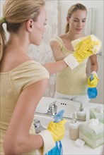 Woman cleaning mirror in bathroom.