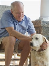 Senior man sitting on porch with dog.