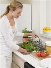 Woman washing vegetables in kitchen sink.