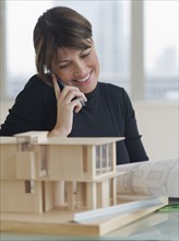 Architect talking on cell phone next to building model.