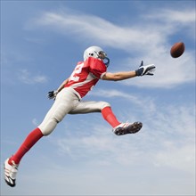 Football player in mid-air reaching for football. Date: 2008