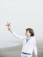 Girl holding starfish on beach. Date: 2008
